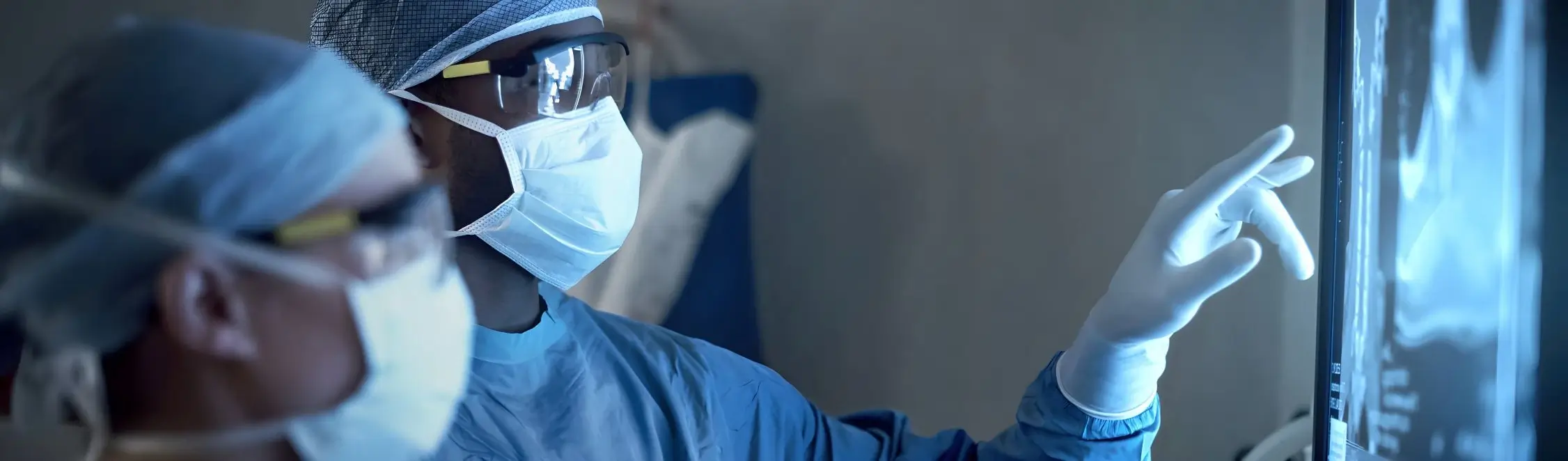 Person mit Mundschutz und Schutzbrille blickt auf ein Display im Labor